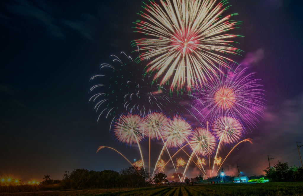 A spectacular firework display illuminates the night sky, with colorful explosions casting a glow over open fields and distant city lights.