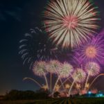 A vibrant firework display lights up the night sky with colorful bursts of red, green, and purple above a field.